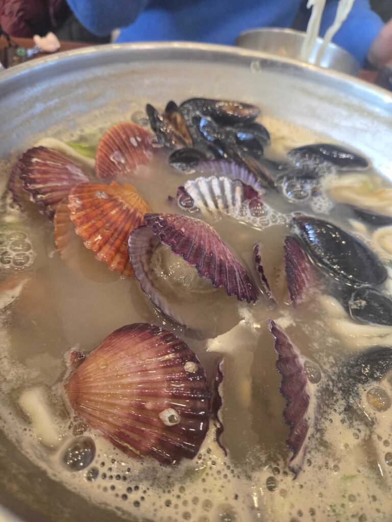 Scallops and mussels cooking in the milky kalguksu broth close-up