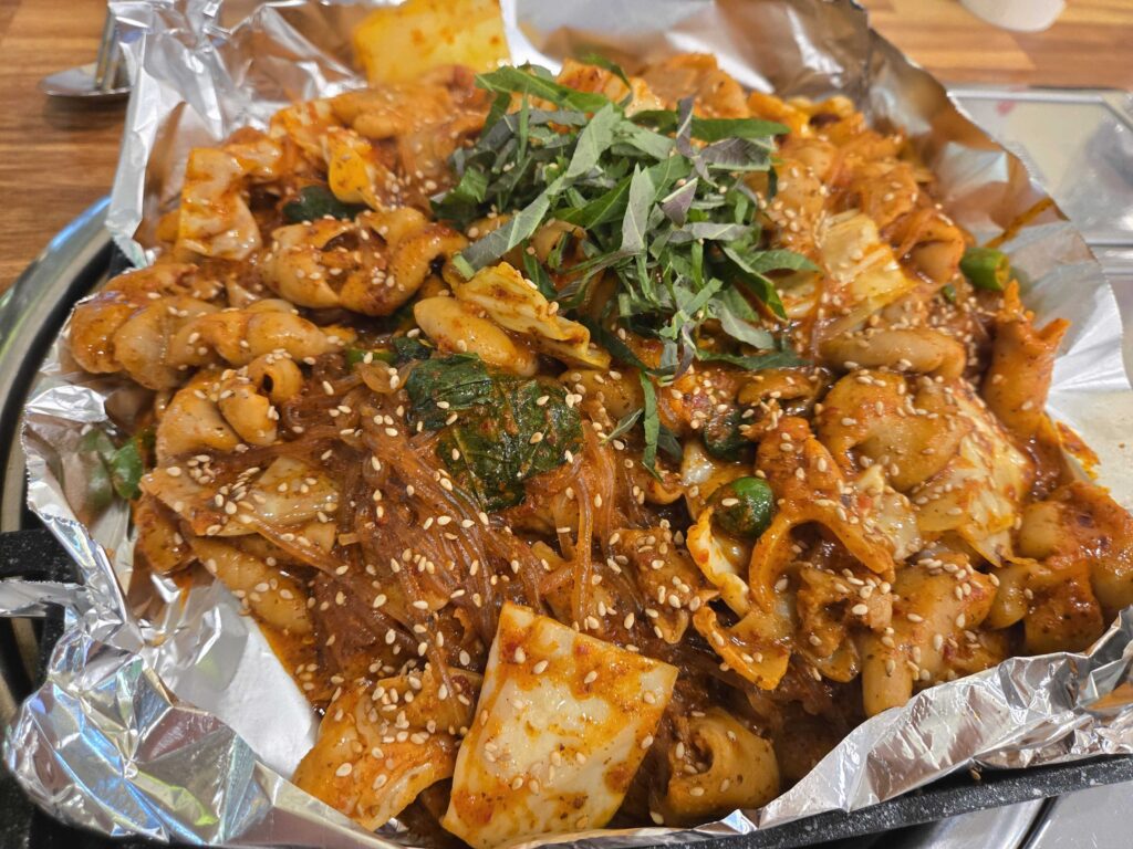 Close-up of spicy Korean intestine stir-fry with vegetables, sesame seeds, and rice cakes