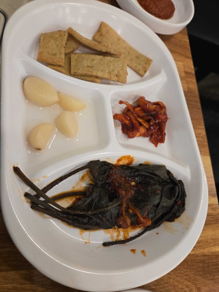 Korean banchan side dishes including garlic cloves, kimchi, dried seaweed, and crackers