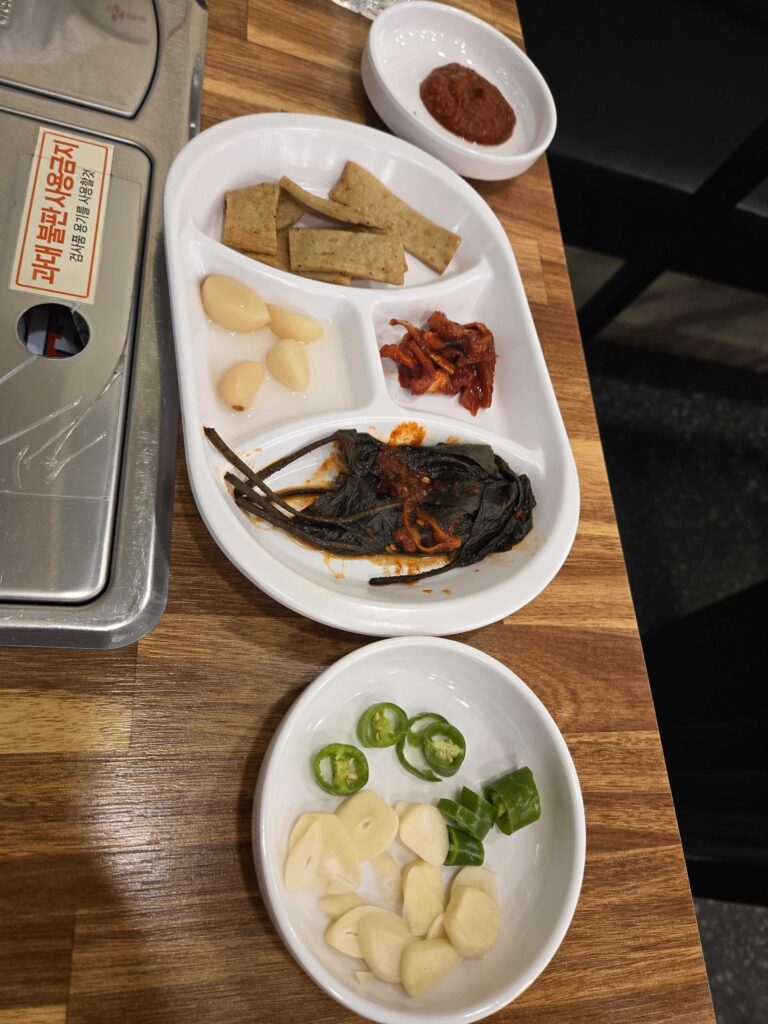 Restaurant table setup with banchan side dishes, ssamjang sauce, and tabletop gas burner