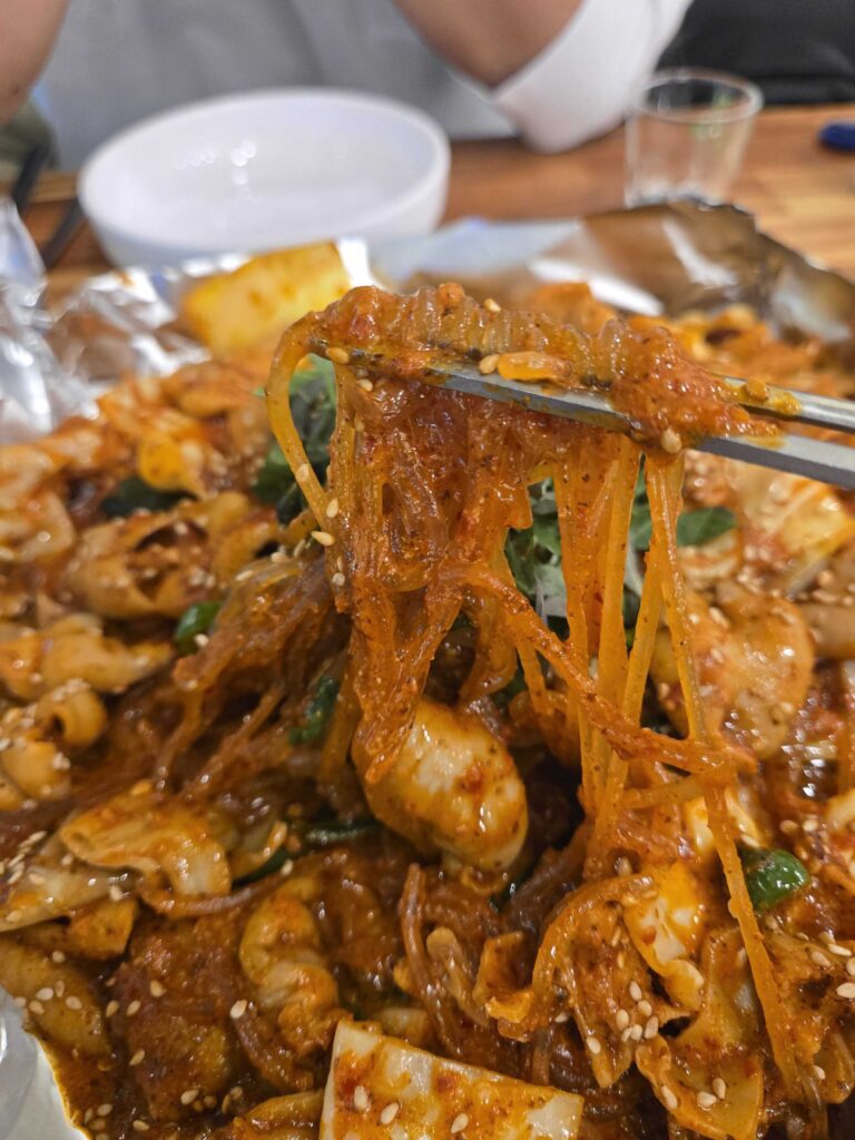 Lifting glass noodles and intestines with chopsticks showing rich spicy red sauce