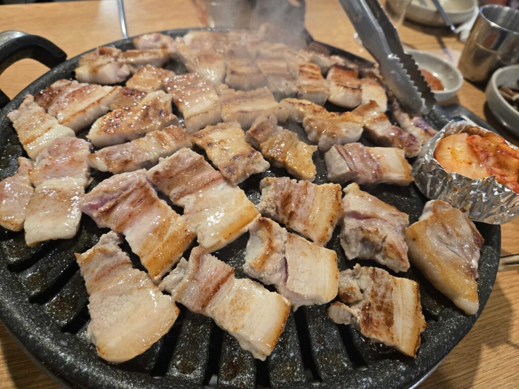 Golden brown crispy samgyeopsal pork belly slices cooking on a hot stone grill plate