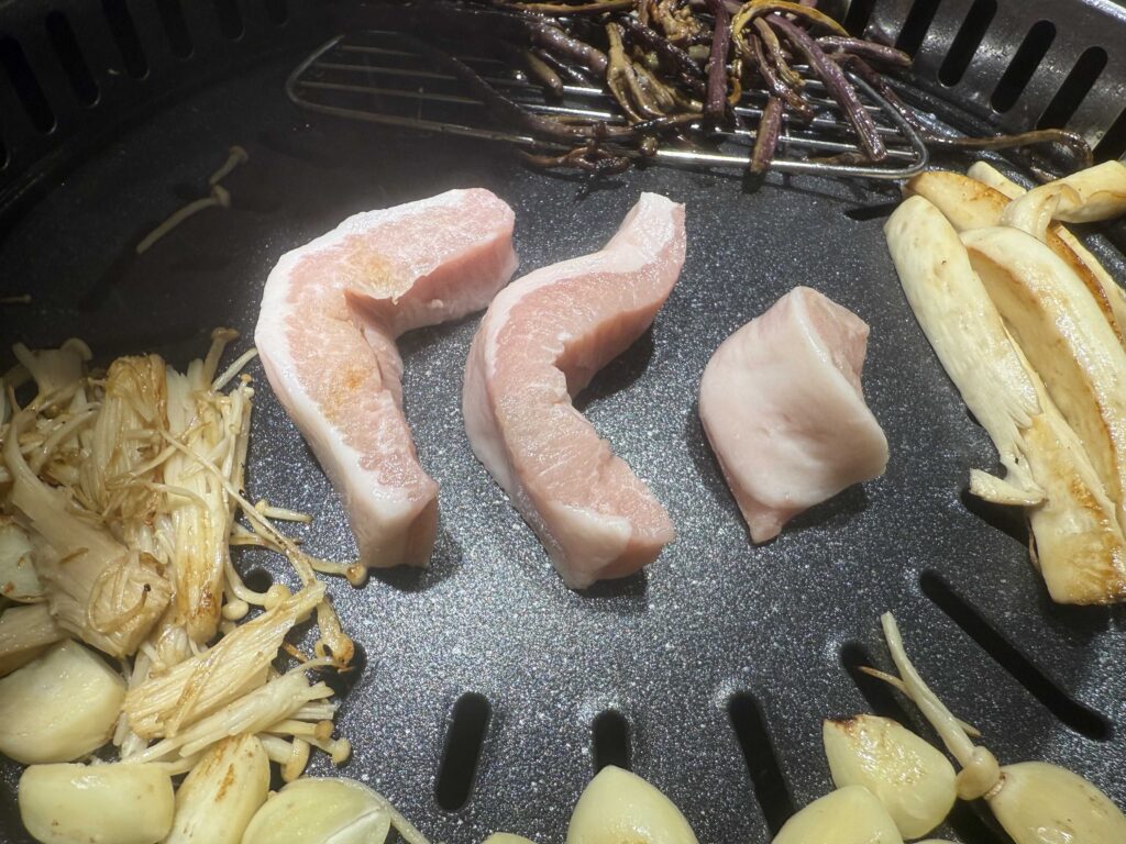 Fresh pork belly samgyeopsal with mushrooms and garlic on the grill at Geobugi Dongnae