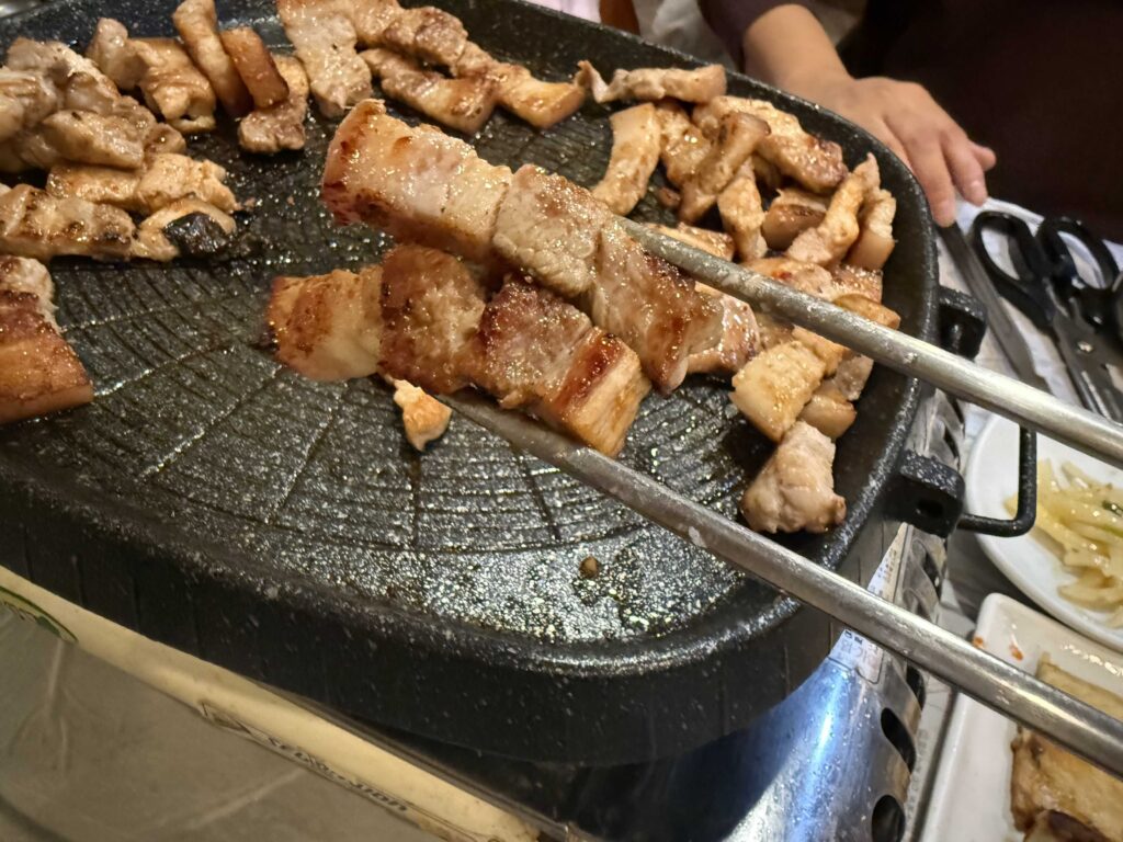 Grilling samgyeopsal pork belly with tongs at Mannajeong Wonju Korea