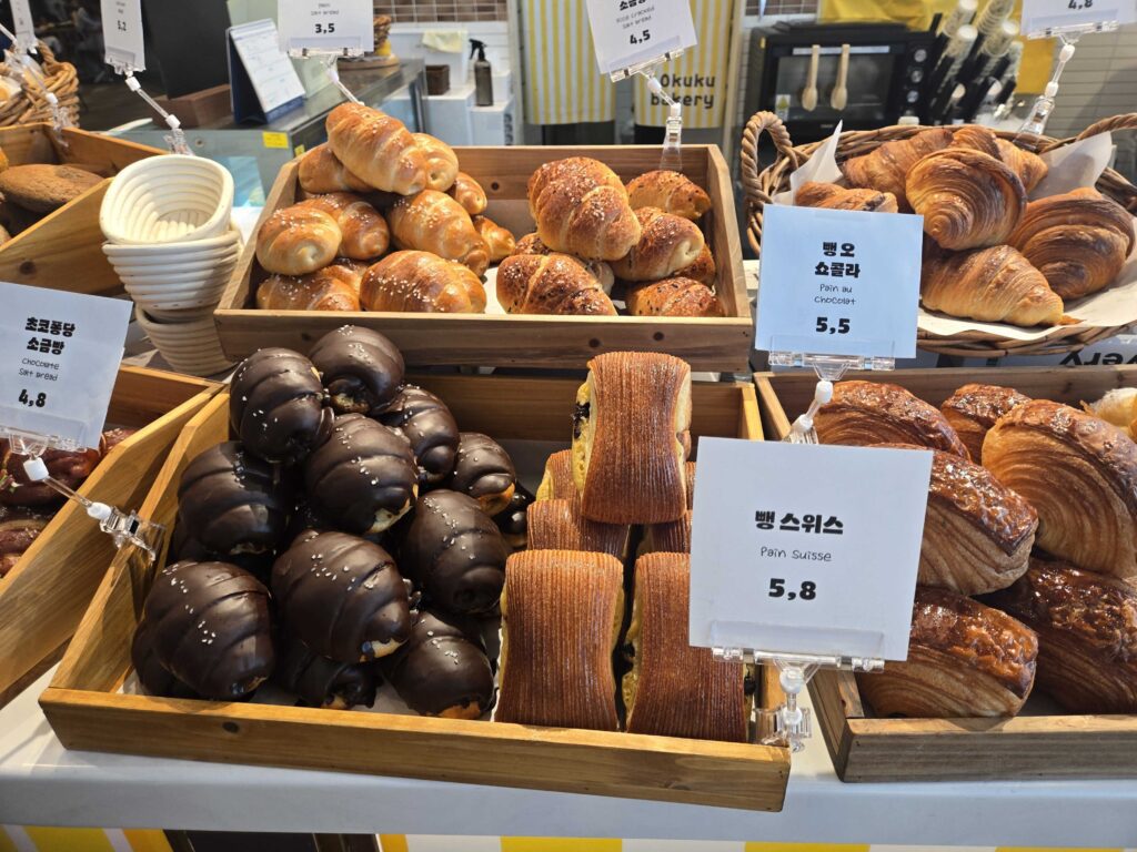 Okuku Bakery display with variety of croissants bagels and signature breads in wooden crates