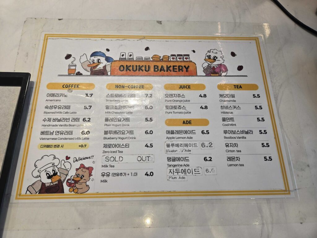 Okuku Bakery drinks menu board showing coffee non-coffee juice tea and ade options with prices