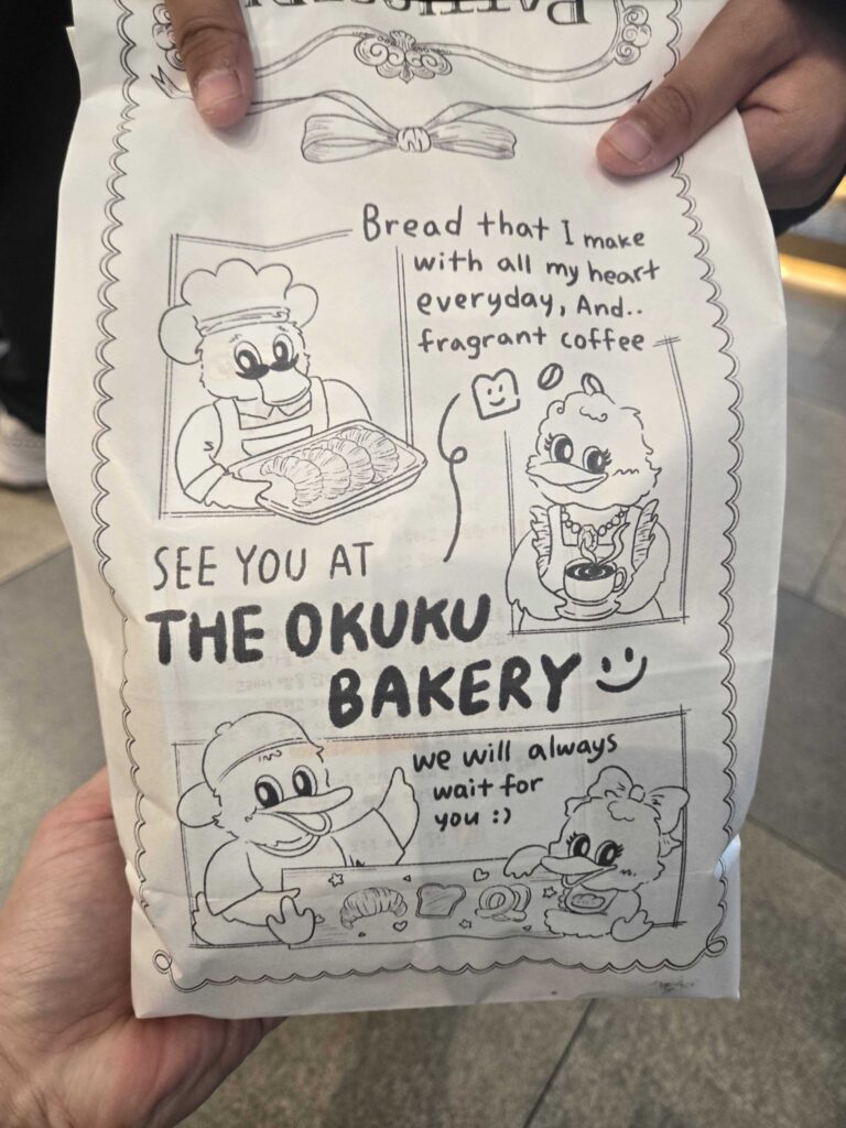 Okuku Bakery illustrated paper bag with SEE YOU AT THE OKUKU BAKERY text and duck characters