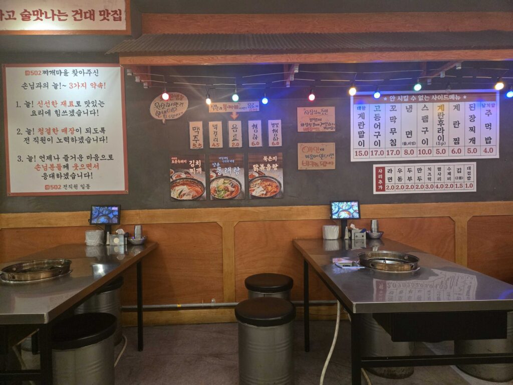 502 Jjigae Maeul full menu board showing stew options side dishes and prices with three promises to customers notice