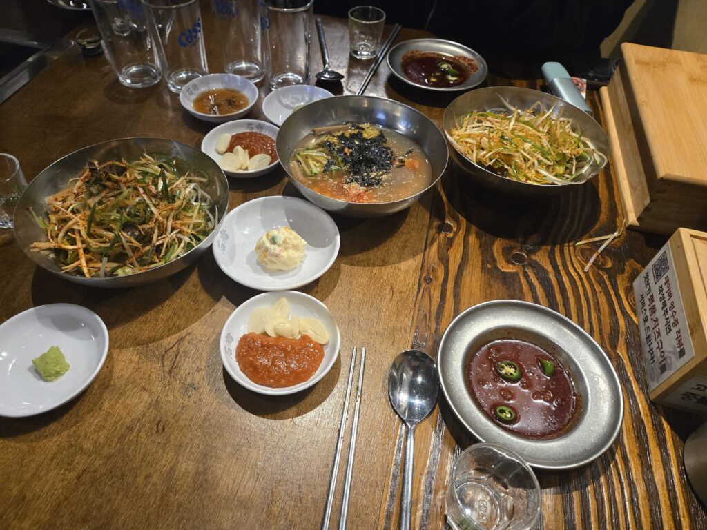 Table spread with Korean side dishes (banchan) at a Korean BBQ restaurant in Seoul — bean sprout namul, potato salad, kimchi sauce, wasabi, soy dipping sauce