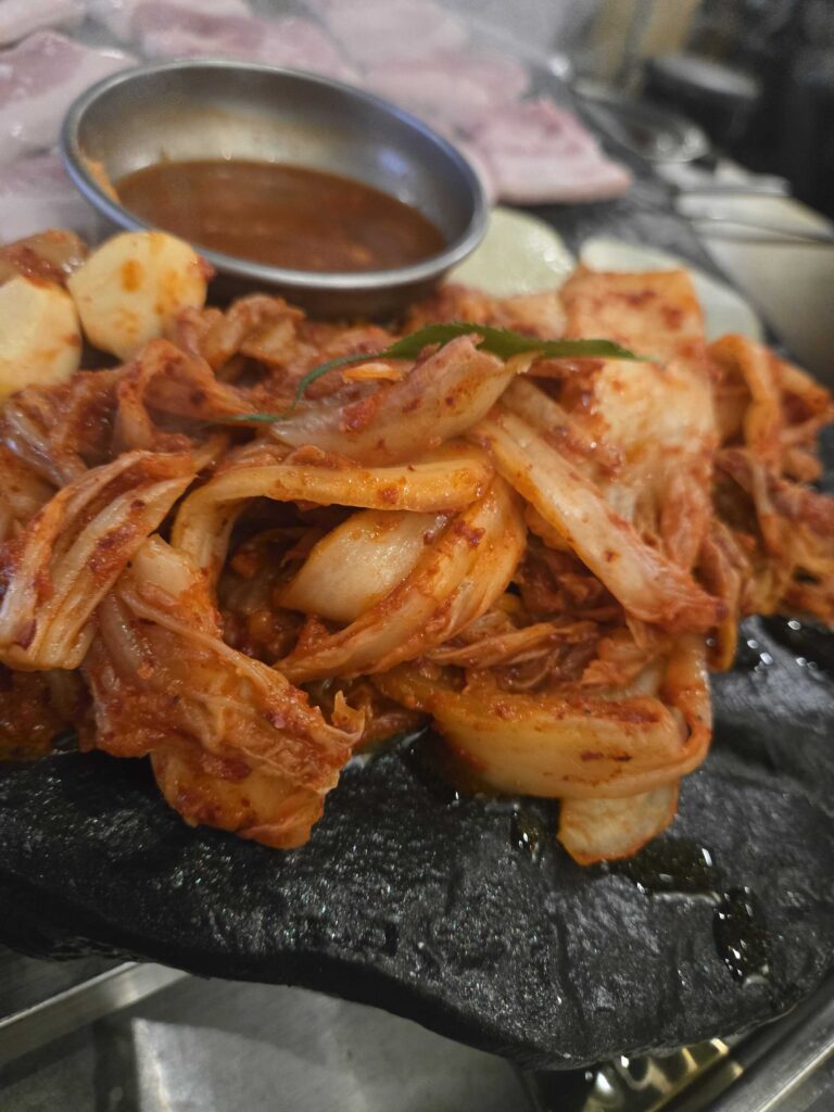 Kimchi and pork belly grilling together on the black stone plate at Seokam Saengsogeum-gui Seongsu, with doenjang paste sauce in the center
