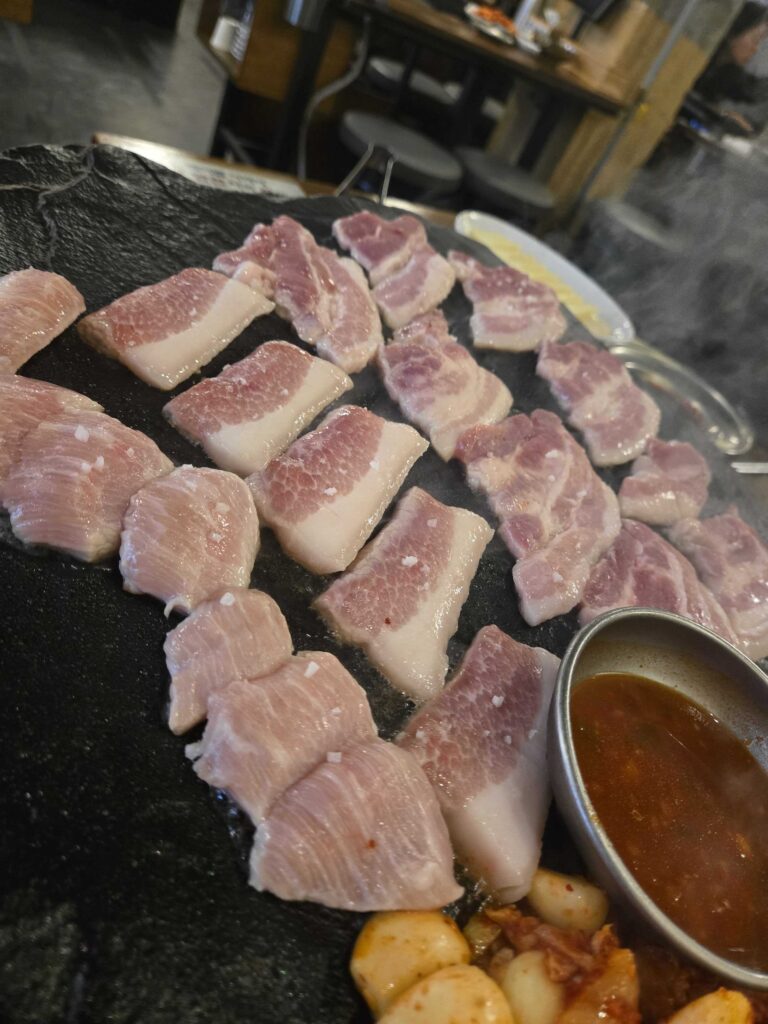 Pork belly slices on the hot black stone grill plate at Seokam Seongsu, with doenjang dipping sauce and kimchi on the side
