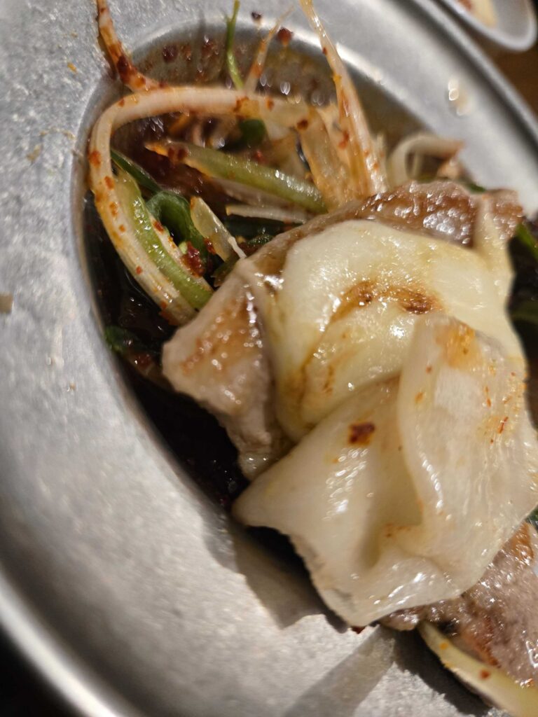 Close-up of perfectly grilled pork belly with garlic on a stone grill plate — beautifully browned and juicy