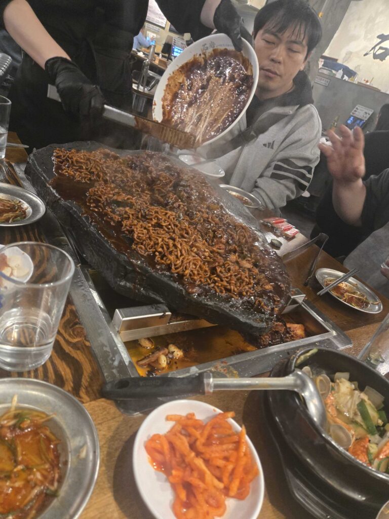 Staff pouring chapagetti (짜파게티) black bean noodles directly onto the stone grill after the pork at Seokam Saengsogeum-gui Seongsu