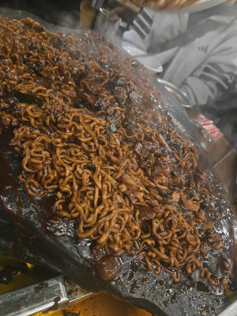 Close-up of chapagetti (짜파게티) grilled on the stone plate at Seokam Saengsogeum-gui Seongsu — smoky, crispy black bean noodles