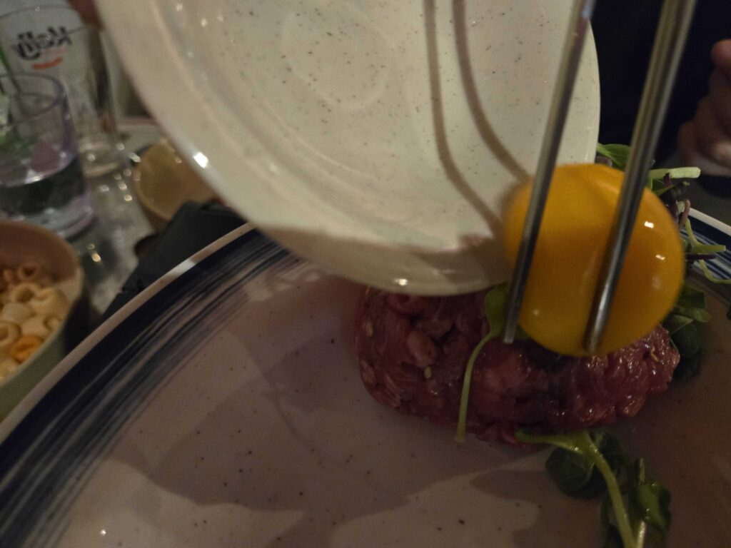Pouring egg yolk over yukhoe beef tartare at Guwoldong Kkachine