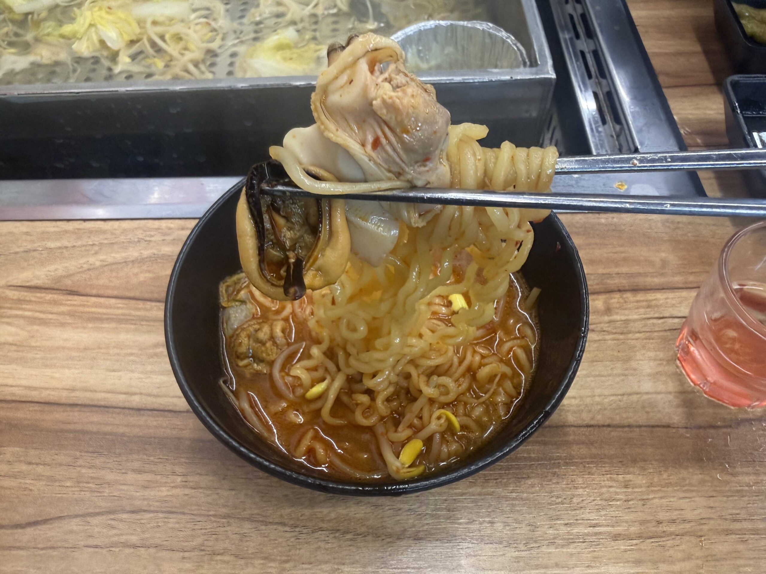 Chopsticks pulling up noodles and abalone from Jjimagi Jamsil Bangi haejang ramyeon