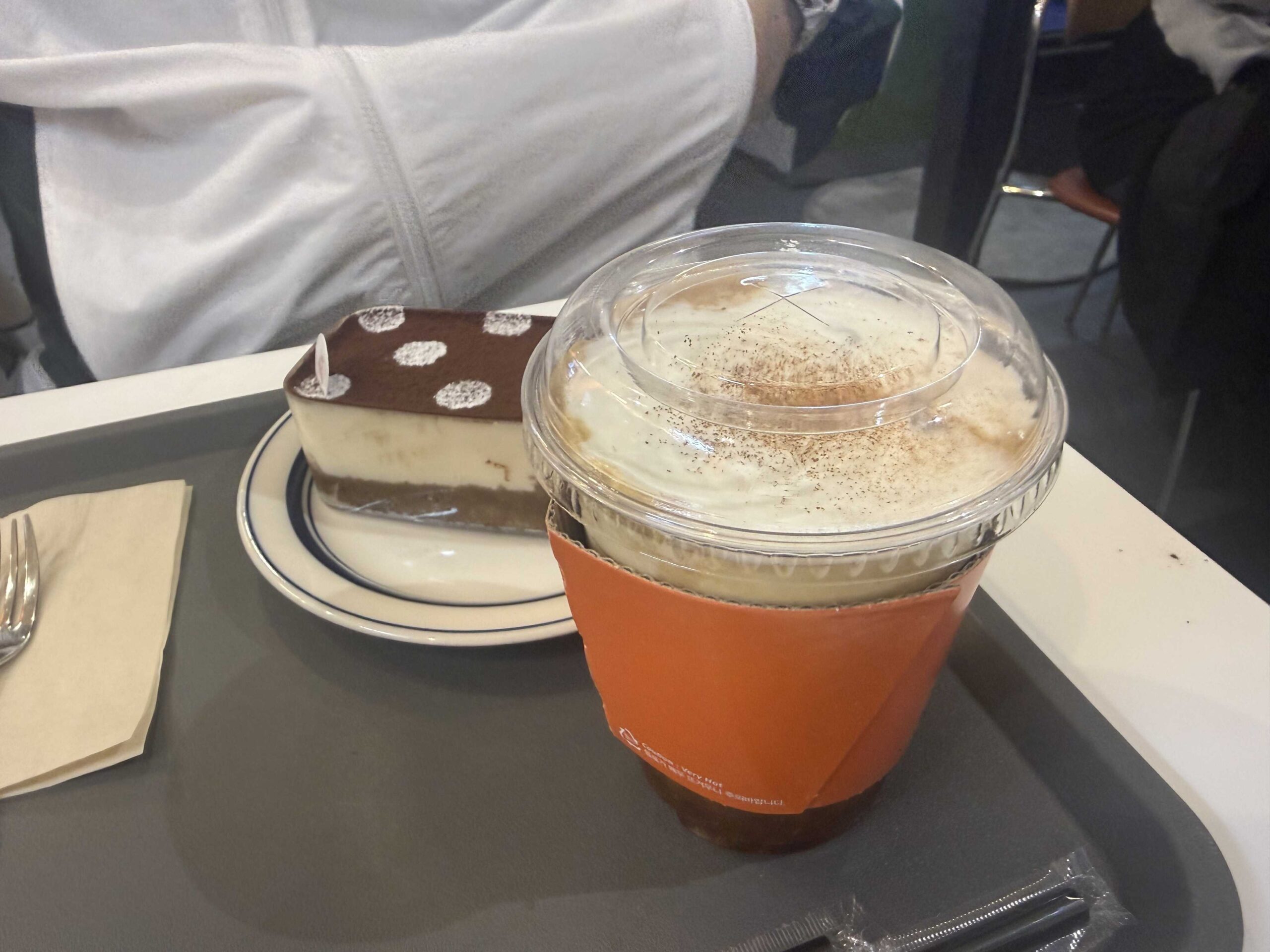Petit Chlo Jamsil cream latte in orange sleeve next to tiramisu cake