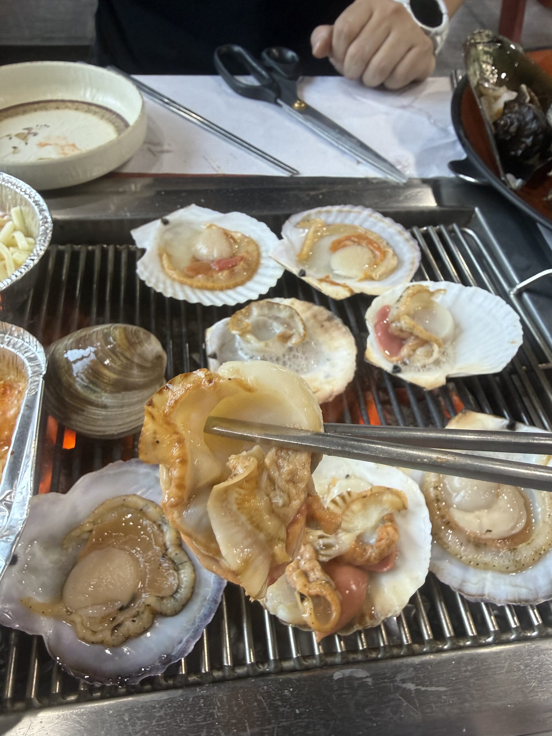 Family lunch table with grilled scallops and naktji tangtangi at Pungnyeon Hwesenta
