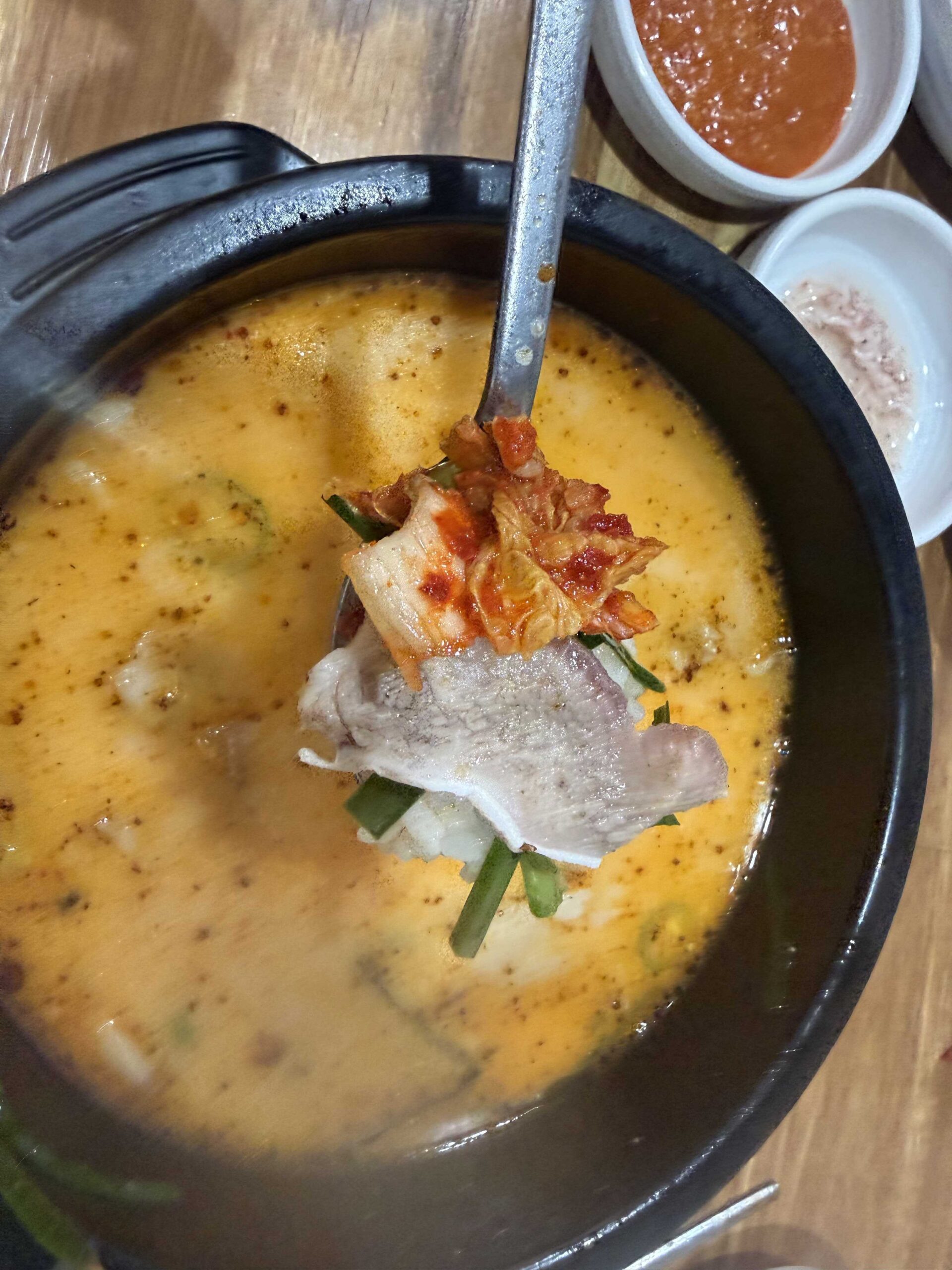Close-up of beef and kimchi on a spoon in Dukkeobi Sundae Guk Hanam red broth