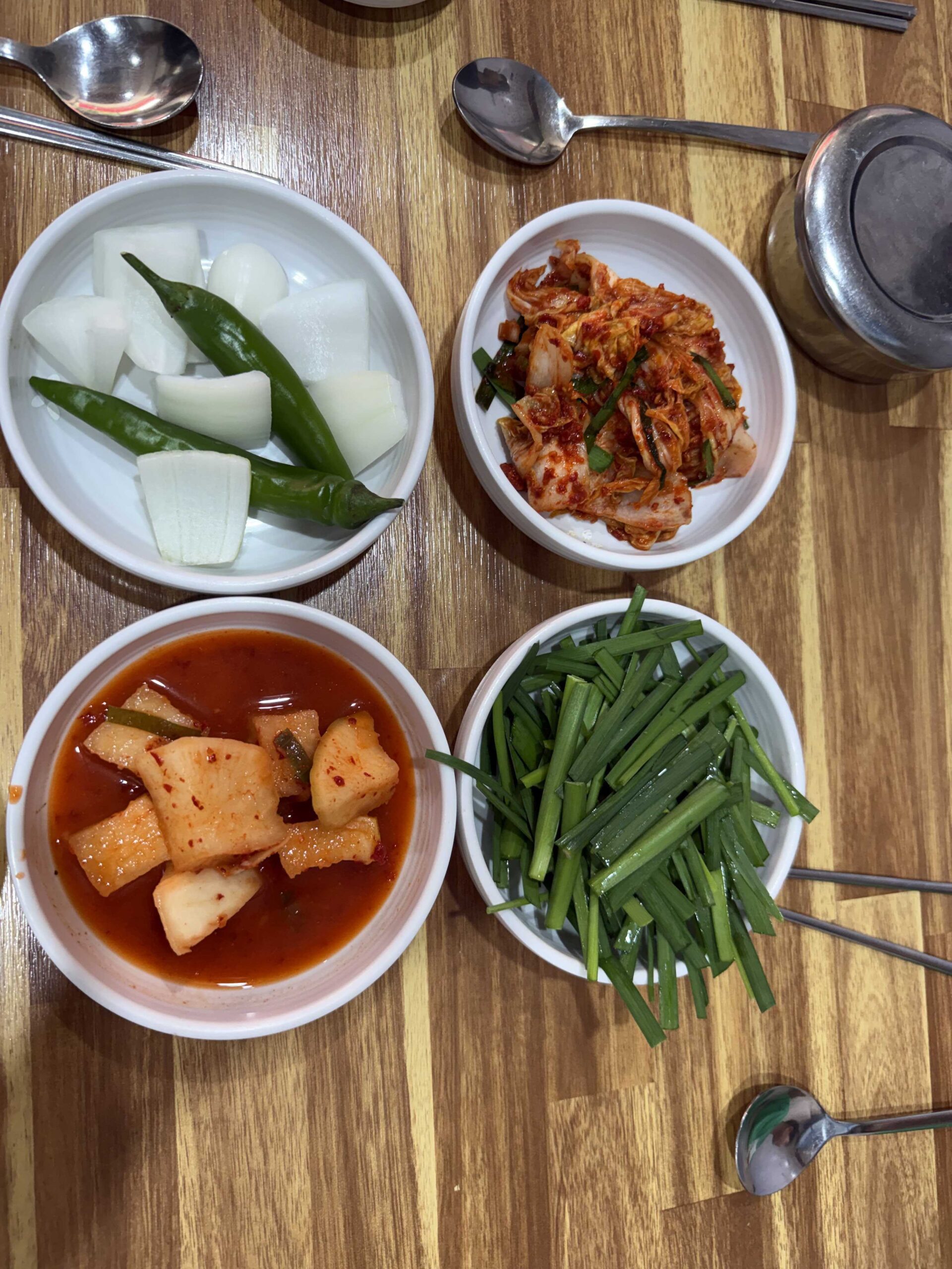 Four side dishes plated at Dukkeobi Sundae Guk Hanam with kimchi pickled radish chili and chives