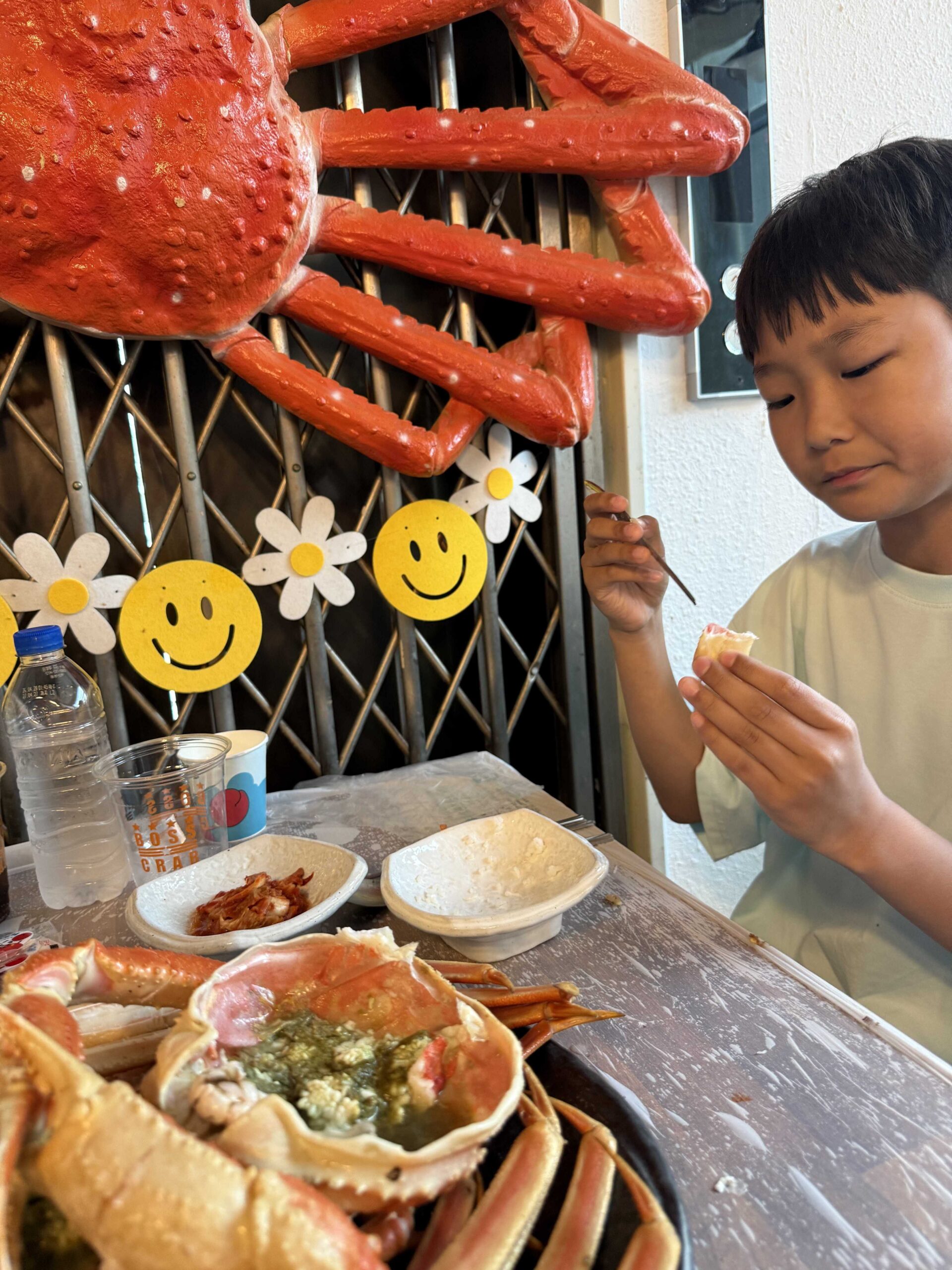 Boy eating snow crab meat under the giant crab decor at Boss Daege Samcheok