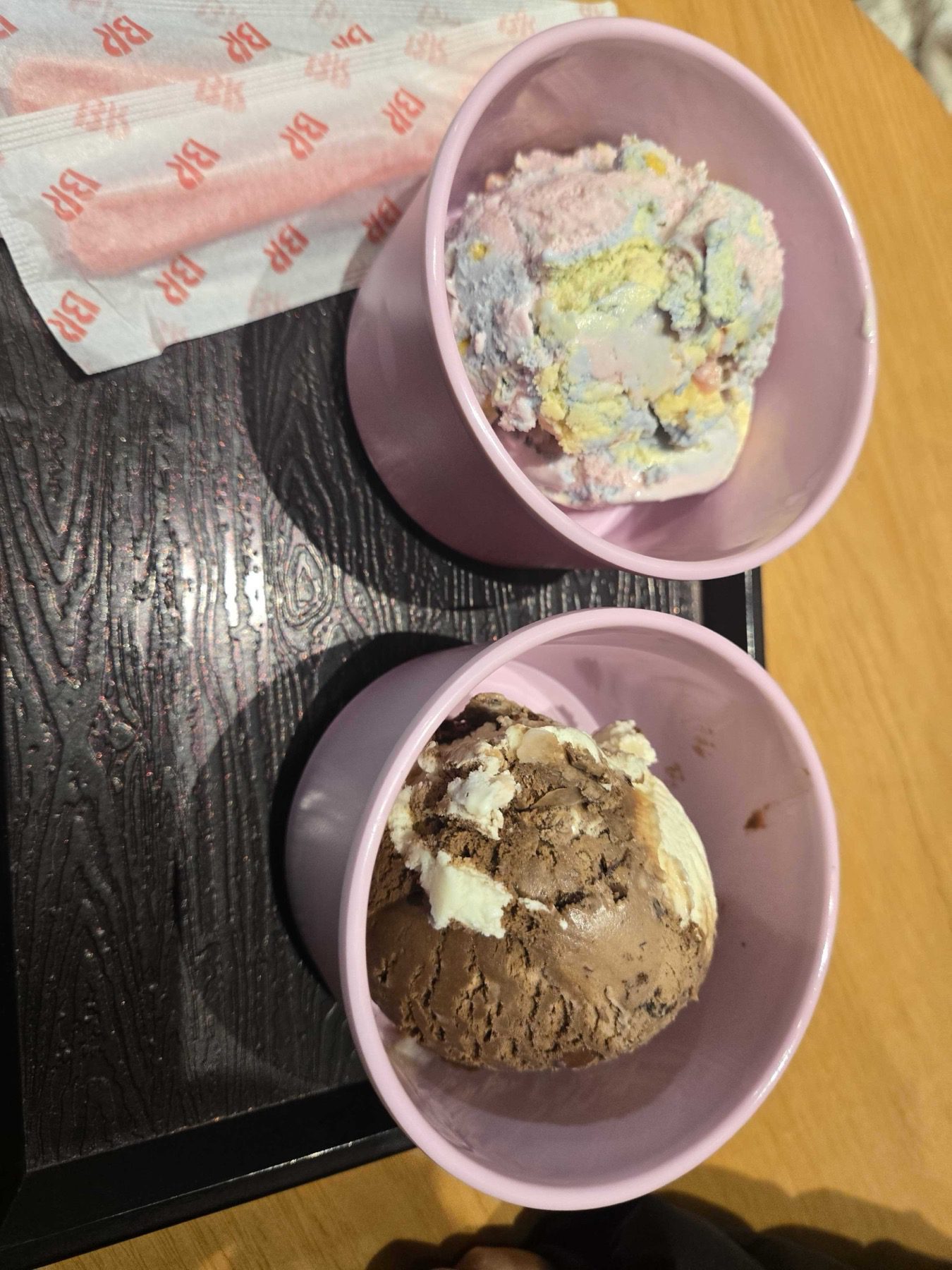 Two single scoops in pink bowls on a black tray with BR spoons