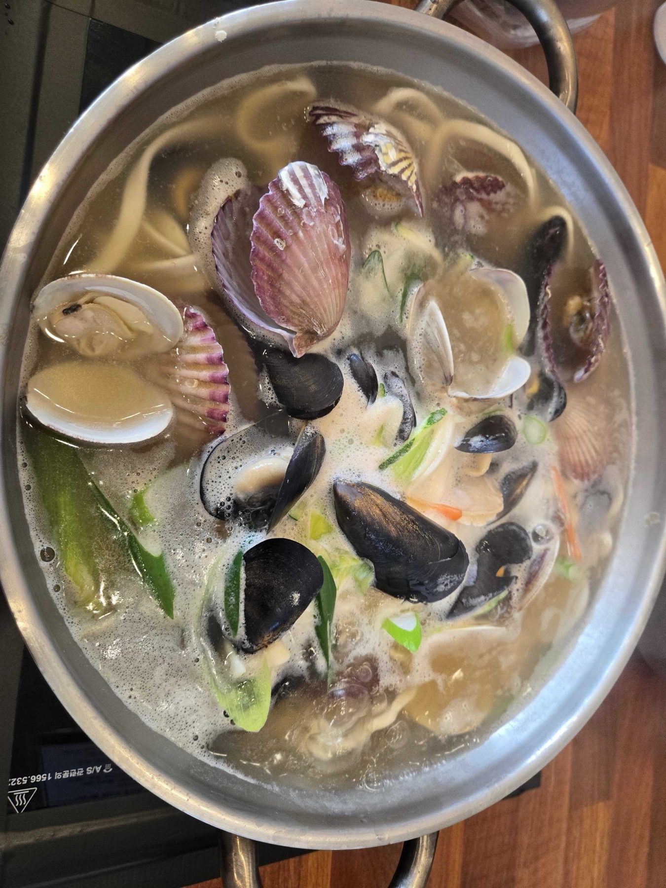 Park Seung-gwang kalguksu pot at full boil with scallops mussels clams and noodles visible