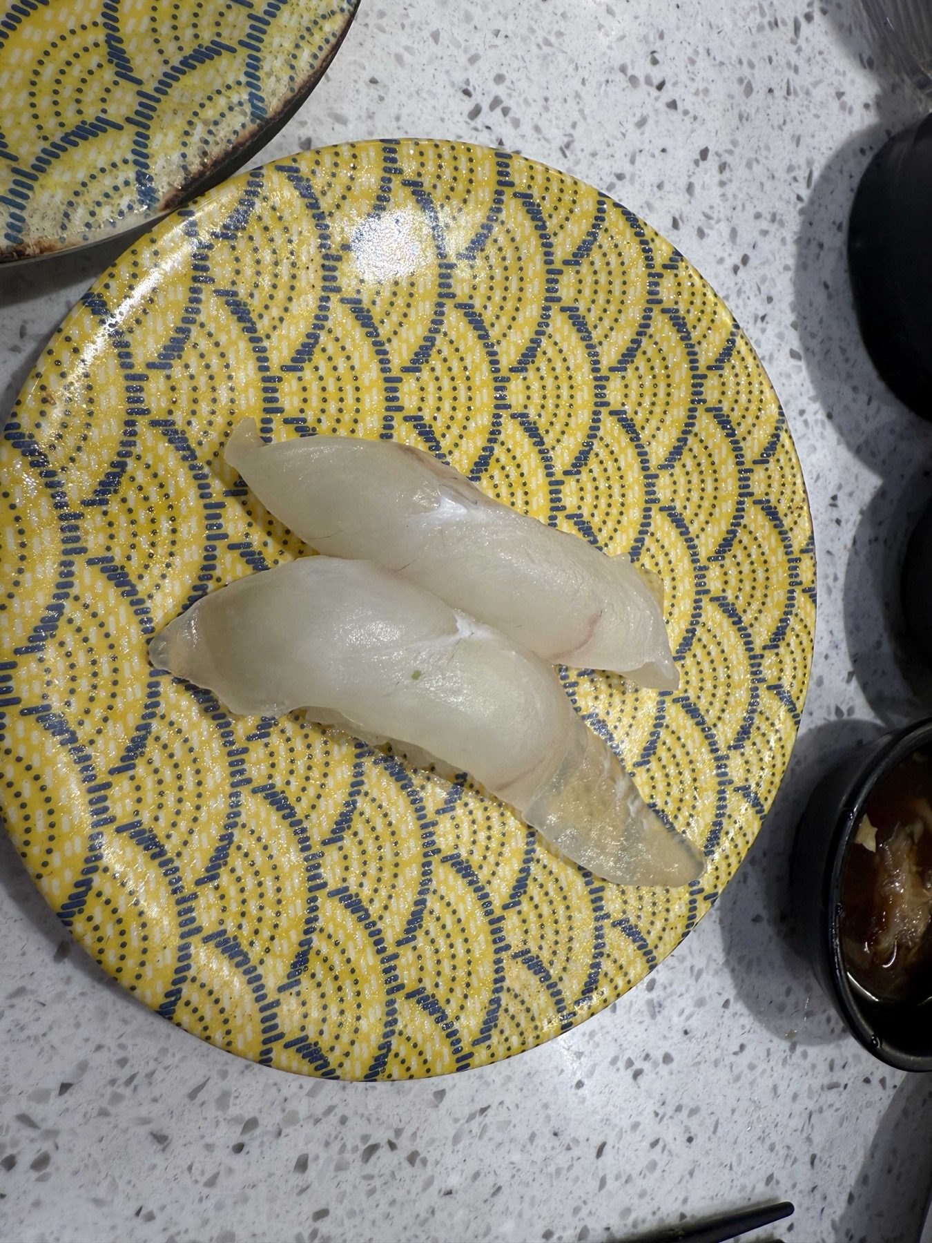 Two translucent white fish nigiri on a yellow wave-pattern plate at Sushi Ian Wirye