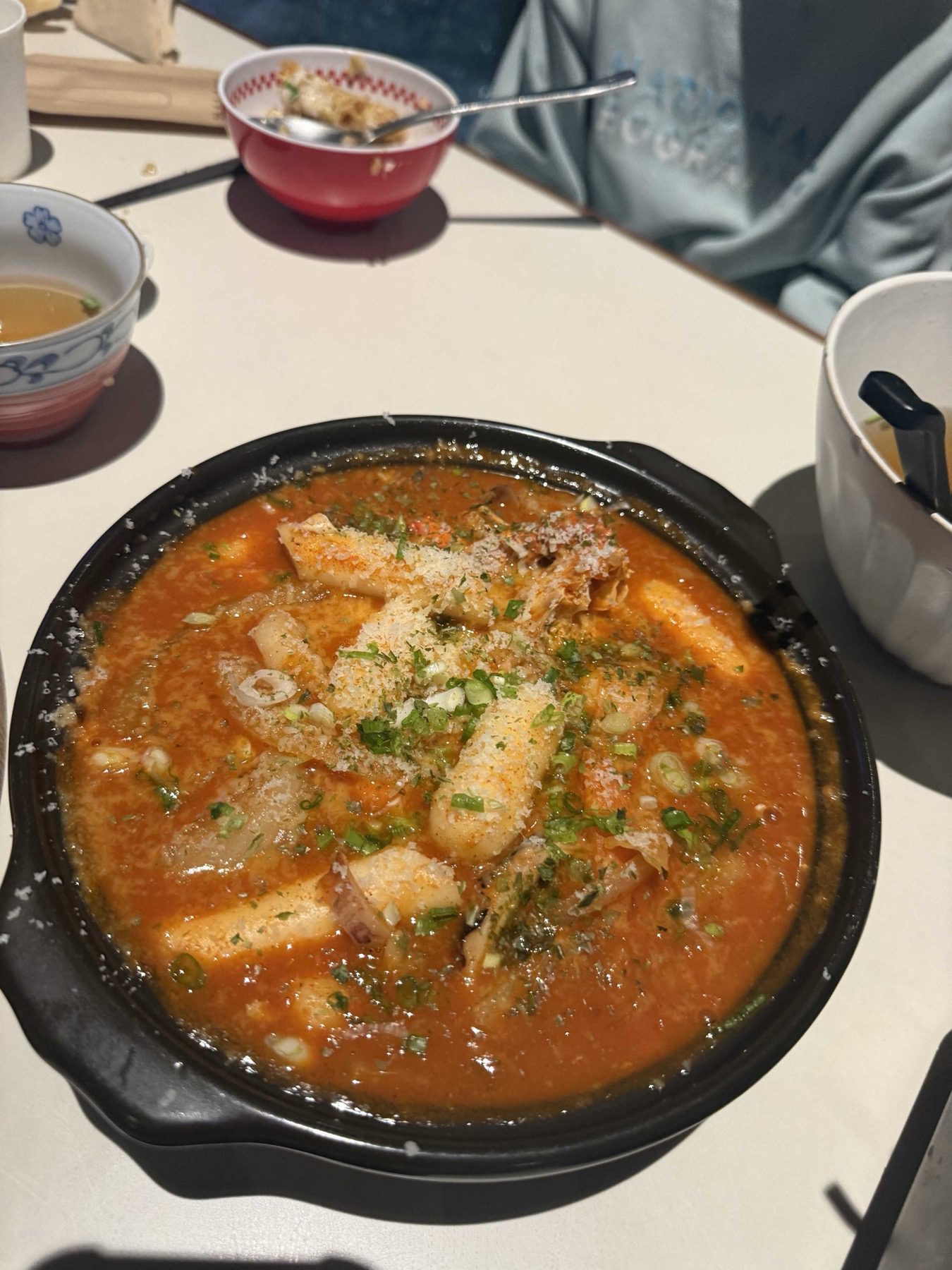 Broth tteokbokki in a black pot topped with grated cheese, herbs and scallions at YONEZ Hanam