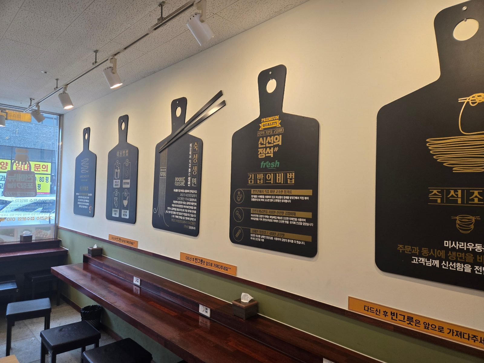 Long wooden counter with stools and wall boards inside Misari Udon Gamil