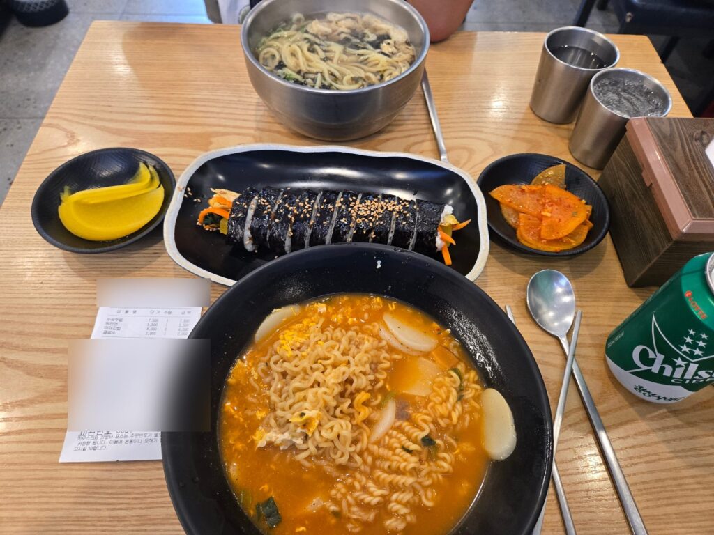 Handmade udon, tteok-ramyeon, vegetable kimbap, danmuji and radish kimchi on a wooden table