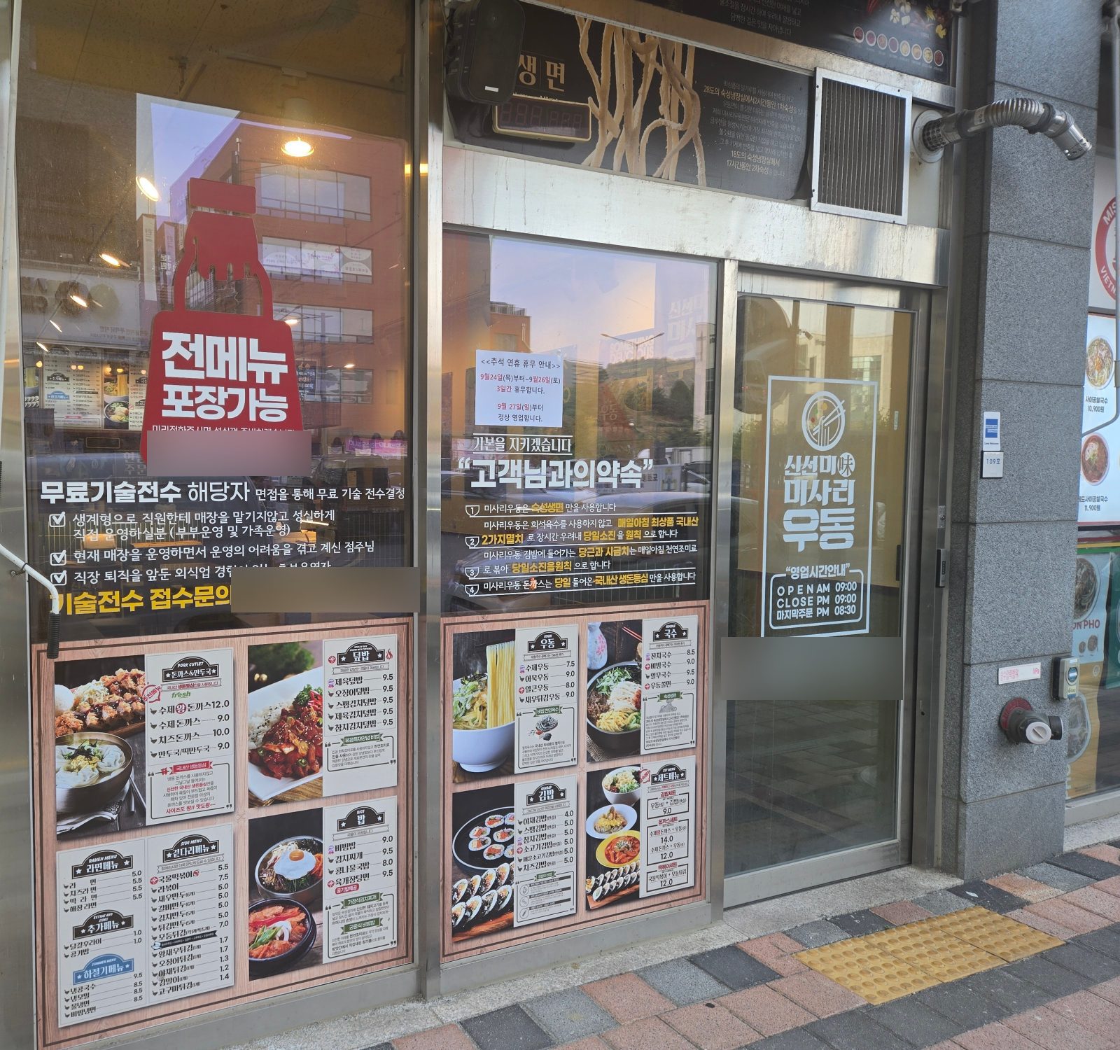 Menu boards and opening hours on the front window of Misari Udon Gamil