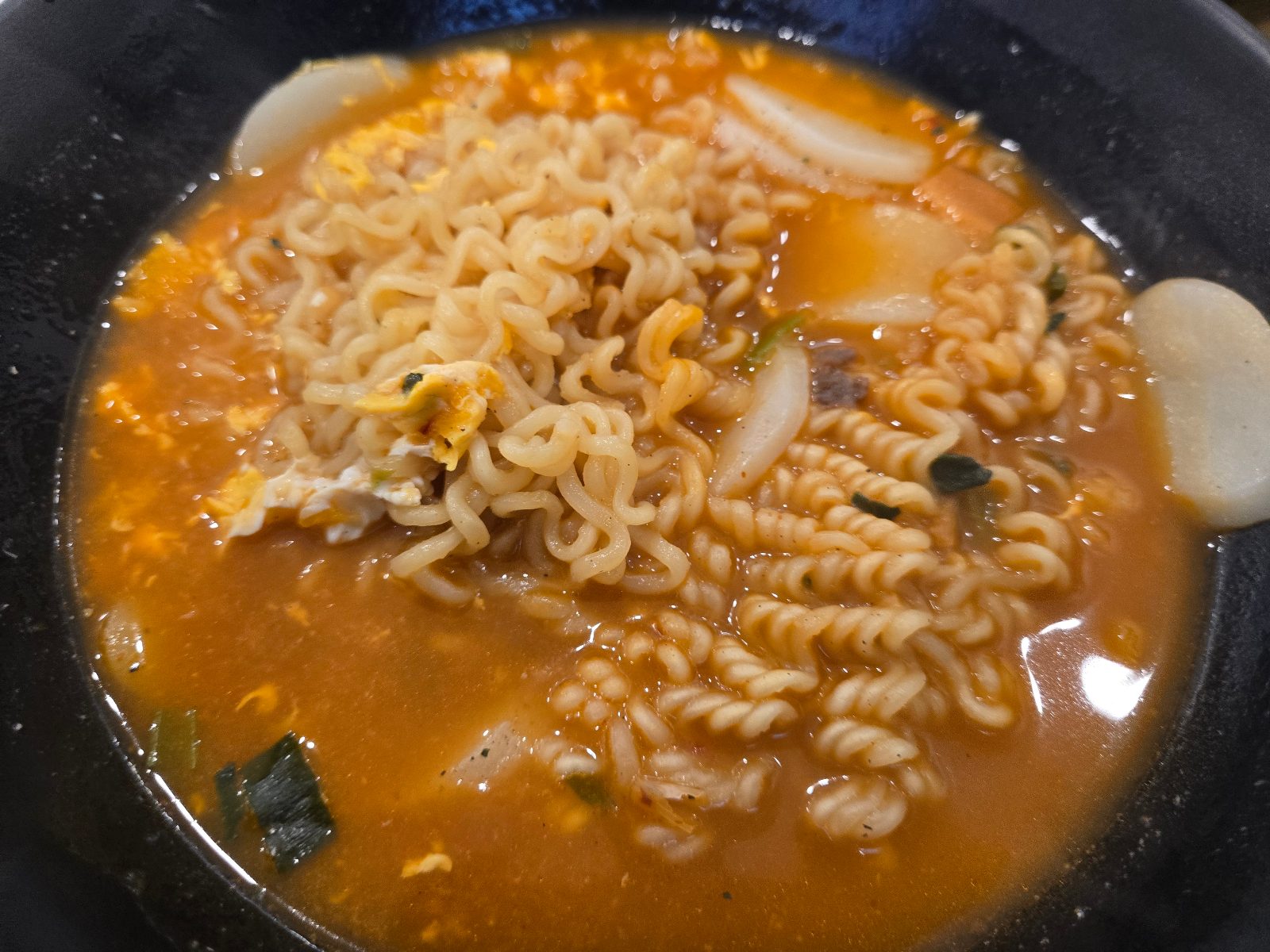 Tteok-ramyeon with egg, sliced rice cakes, wavy and spiral noodles in orange broth