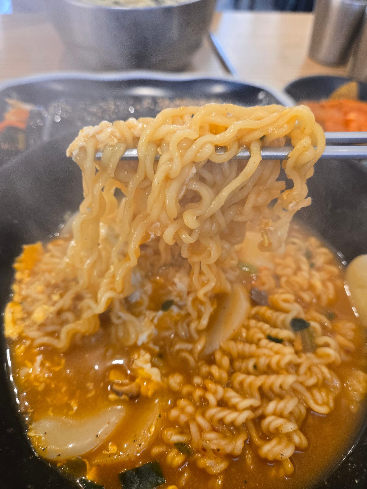 Wavy instant noodles lifted with chopsticks over the tteok-ramyeon bowl