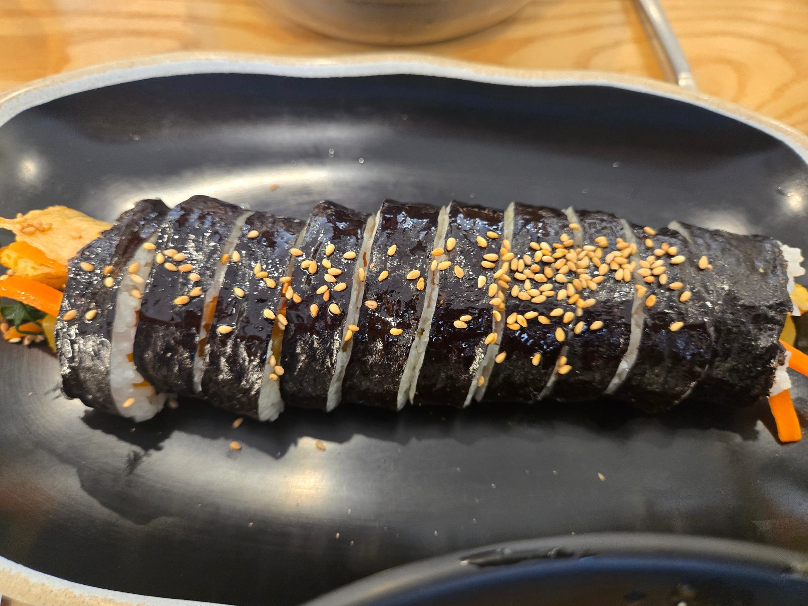 Sliced vegetable kimbap roll topped with sesame seeds on a black plate