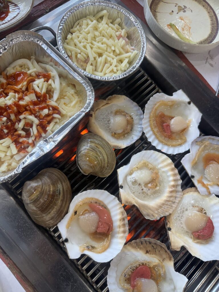 Scallops and clams on the grill, with foil trays of cheese
